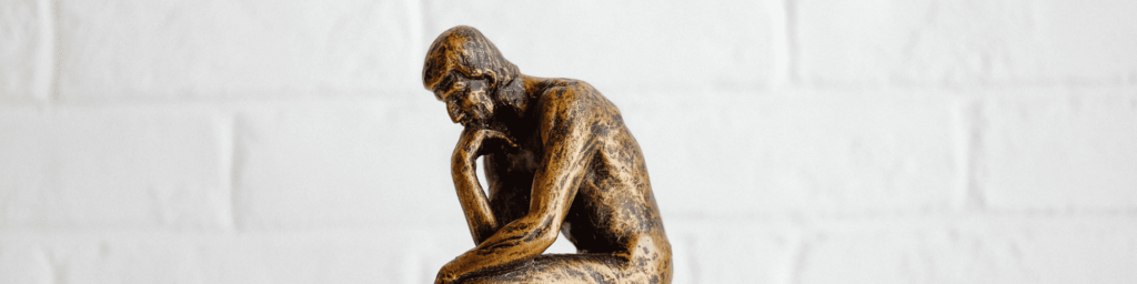 Statue "The Thinker" in bronze in front of white brick background - cultivating curiosity